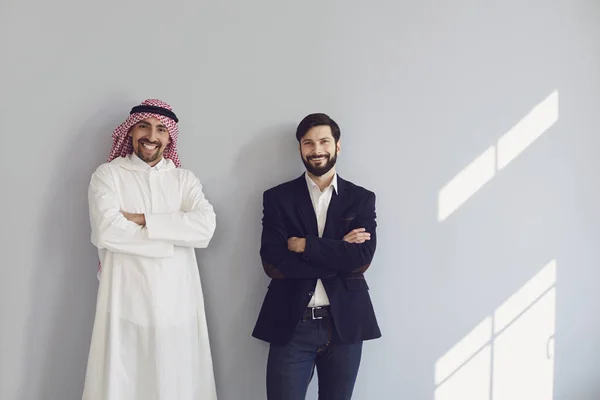 Арабские и европейские бизнесмены стоят и улыбаются на сером фоне. — стоковое фото