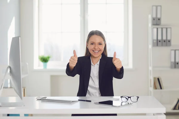 Smiling businesswoman raised her thumb up while sitting at a table in the office. — Stock Photo, Image