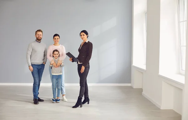 Emlakçı kadın yeni evinde panosu ve ailesiyle gülümsüyor. — Stok fotoğraf