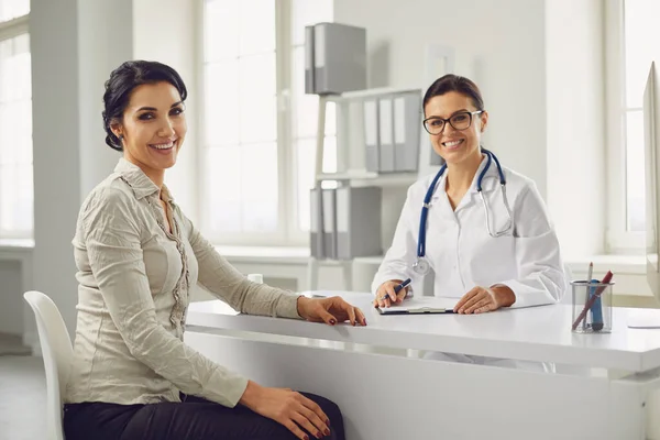 Lächelnde Patientin bei Konsultation mit Ärztin am Tisch in Praxisklinik. — Stockfoto