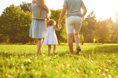 Mutlu bir aile yaz parkında çimlerin üzerinde yürüyor. Anne baba ve çocuklar doğada oynuyorlar..