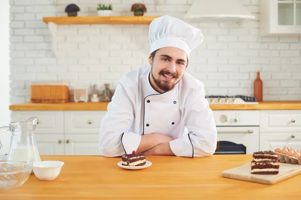 Konditor lächelt, während er mit Kuchen in der Hand in der Küchenbäckerei steht — Stockfoto