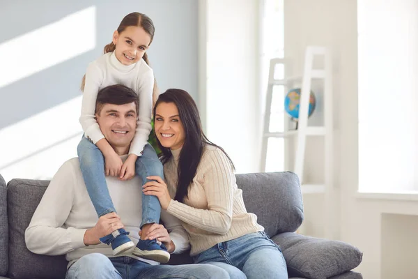 Szczęśliwa uśmiechnięta rodzina. Córka siedzi na ramionach ojców, a matka siedzi na kanapie. — Zdjęcie stockowe