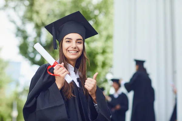 Egy fiatal női diplomás a háttérben az egyetemi diplomások. — Stock Fotó