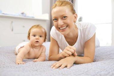 Mutlu anne odada yatakta oturan bebek gülümsüyor.
