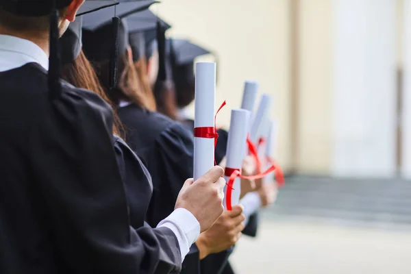 Scrolls of diplomas in the hands of a group of graduates. — Stock Photo, Image