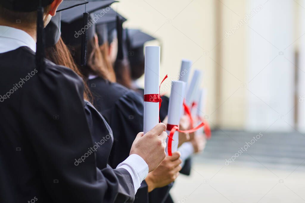 Scrolls of diplomas in the hands of a group of graduates.