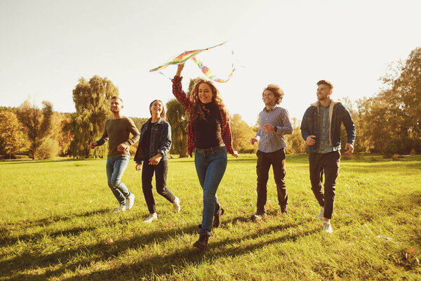 Young people with a kite run on the grass in the park.