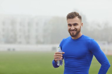Athletic man with a bottle of water in training at the stadium.