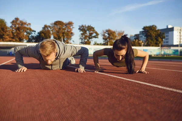 Young couple doing pushups in the stadium — Stock Photo, Image