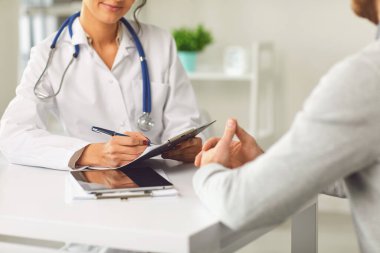 Female doctor therapist gross allergist nutritionist otolaryngologist and male patient sitting at a table in a clinic office