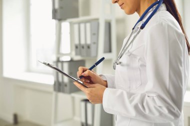 Yüzsüz doktor kadın klinikte beklerken panoya reçete yazıyor..