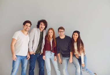 Gri arka planda gülümseyen günlük kıyafetler içindeki bir grup genç..