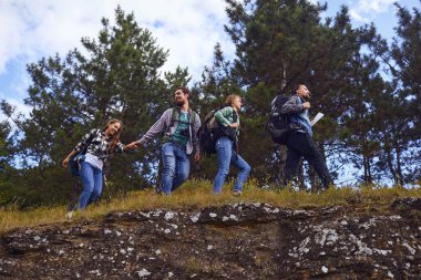 Sırt çantalı gençler ormanda yürüyor.