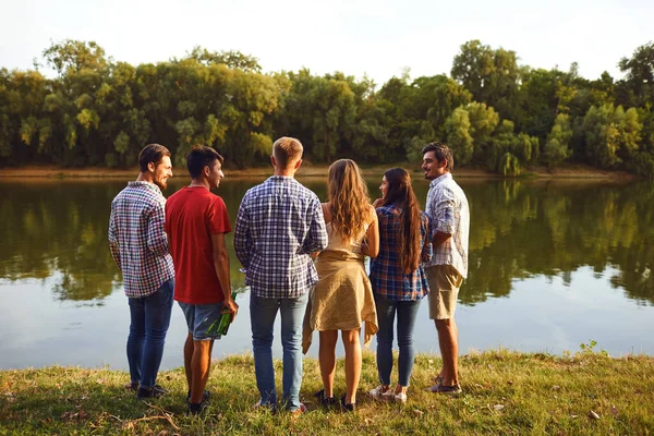 Back view a group of young people resting, communicates on the lake — Stock Photo, Image