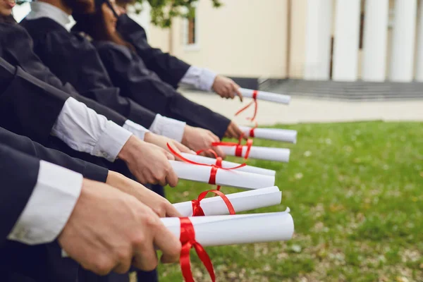 Scrolls of diplomas in the hands of a group of graduates. — Stock Photo, Image