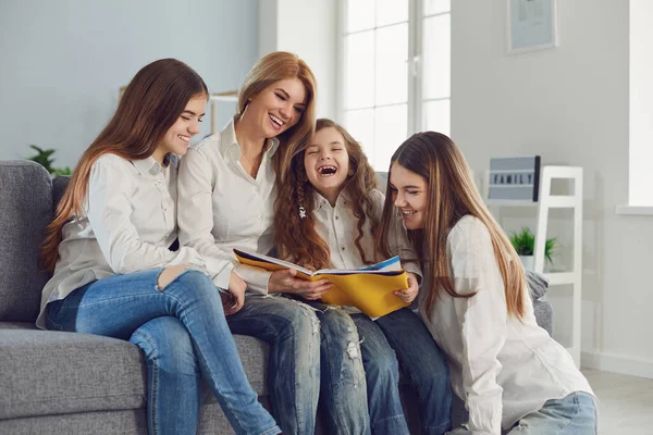 Madre con bambini legge un libro seduto su un divano in una stanza . — Foto Stock