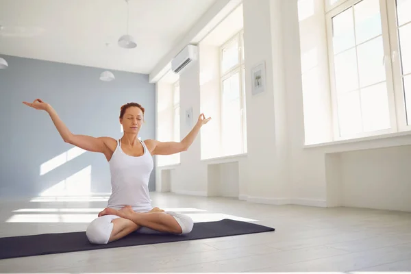 Chica del yoga. Mujer fitness en ropa deportiva blanca sentada en una pose de yoga medita se relaja sentada en el suelo en un aula blanca . — Foto de Stock