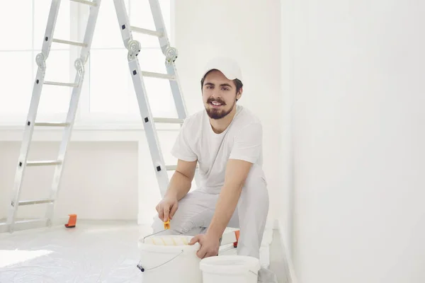 Um pintor masculino de uniforme branco com um rolo trabalha em sua mão em uma sala branca — Fotografia de Stock