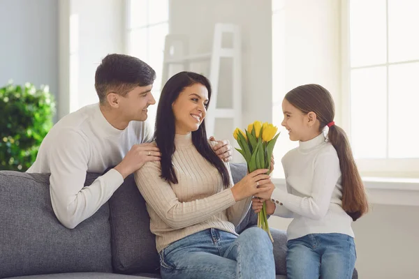 Happy mothers day. Father and baby daughter congratulates mom with flowers and a postcard in a room — Stock Photo, Image