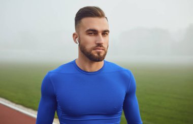Mavi elbiseli bir sporcu siste stadyuma bakarken gülümsüyor.