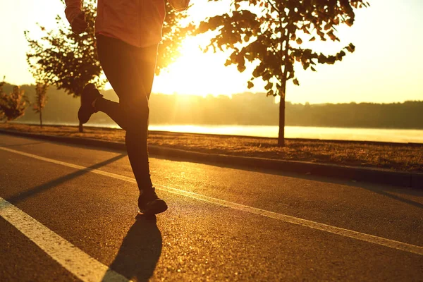 ランナーは秋の公園で日没時に太陽の下で道路を走ります. — ストック写真