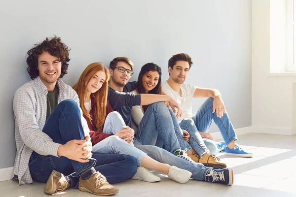 Een groep vrienden zit op de vloer in een kamer op een grijze achtergrond. — Stockfoto