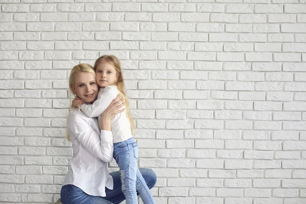 Feliz Páscoa. Mãe e filha com orelhas de coelho sorrindo contra uma parede de tijolo branco . — Fotografia de Stock