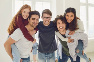 Bir grup arkadaş, gri arka planda bir odada yerde oturuyor..