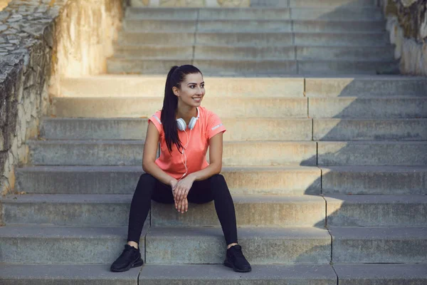 Sports girl resting sitting on the stairs looking at the camera after a workout in park. — Stock Photo, Image