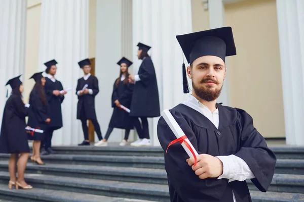 Ein junger männlicher Absolvent vor dem Hintergrund von Universitätsabsolventen. — Stockfoto