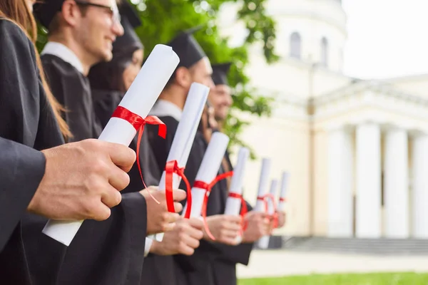 Scrolls of diplomas in the hands of a group of graduates. — Stock Photo, Image