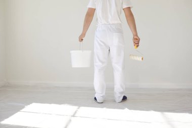 Beyaz üniformalı bir erkek ressam elinde bigudiyle beyaz bir odada çalışıyor.
