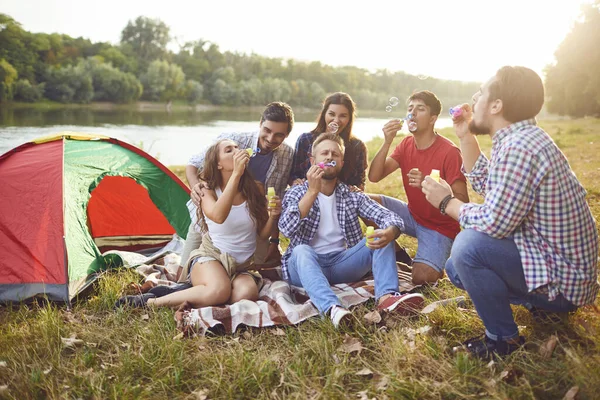 Young people make soap bubbles while sitting on the grass on in nature.