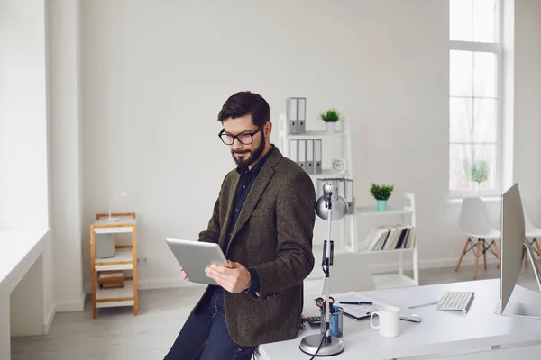 Trabajador de negocios con barba mira la tableta mientras está de pie en la oficina . — Foto de Stock