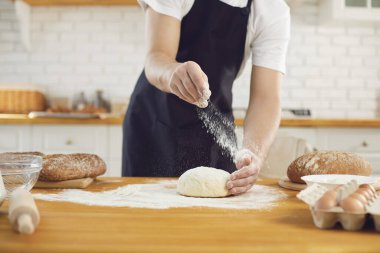 Baker male bearded man makes fresh bread dough at a table in the bakery kitchen.
