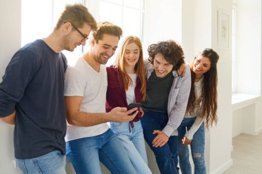 Bir grup mutlu arkadaş telefona bakıp gülüyor parlak bir odada..