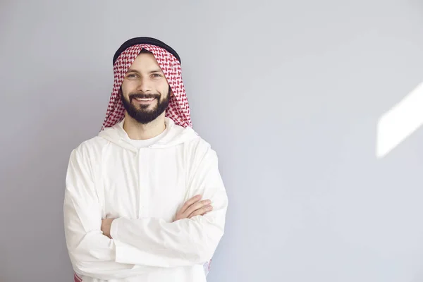 Attractive tersenyum arab man menyeberangi lengannya di latar belakang abu-abu — Stok Foto