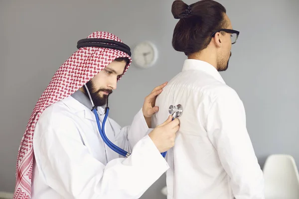 Арабский врач-мужчина слушает в стетоскопе пациента в клинике — стоковое фото