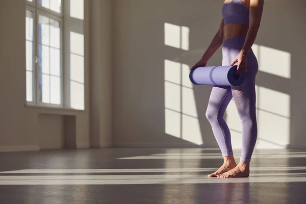 Fitness yoga egzersizi yapan kadın. Elinde yoga minderi olan yüzü olmayan bir kadın parlak bir odada beyaz bir duvara karşı duruyor.. — Stok fotoğraf