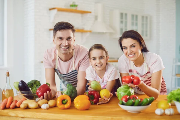 Heureuse famille souriant à une table avec des légumes frais faire de la salade dans la cuisine . — Photo