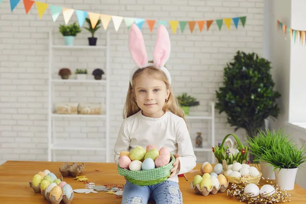 Счастливой Пасхи. Маленькая девочка с кроличьими ушами держит пасхальные яйца в руках в украшенной комнате . — стоковое фото