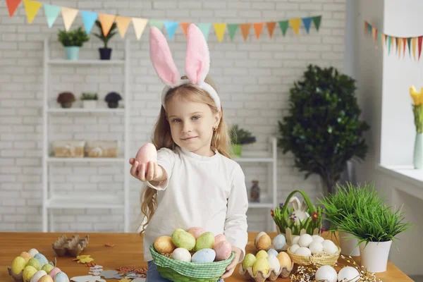 Boldog Húsvétot! Egy nyuszifülű kislány húsvéti tojást tart a kezében egy díszített szobában.. — Stock Fotó