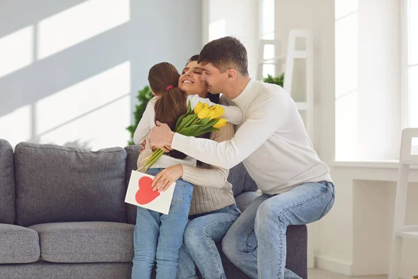 Щасливий день матері. Батько і дочка вітають маму з квітами і листівкою в кімнаті — стокове фото