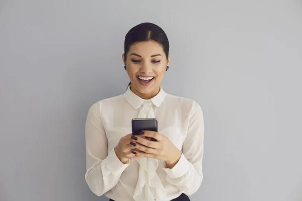 Usar o telefone nas redes sociais. hispânico jovem feliz mulher digitando sms no móvel sorrindo enquanto em pé sobre fundo cinza . — Fotografia de Stock