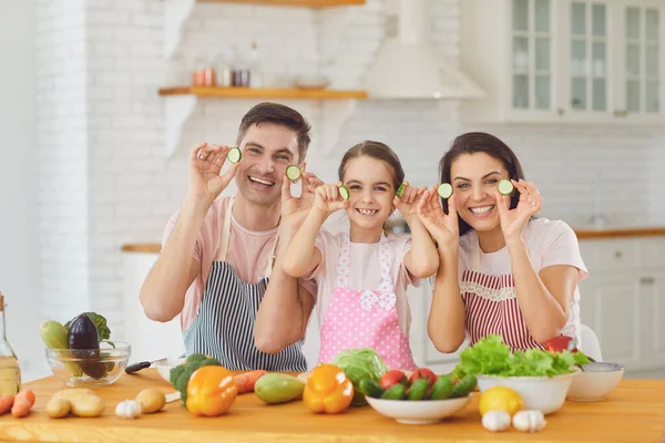 Glad familj ler vid ett bord med färska grönsaker gör sallad i köket. — Stockfoto