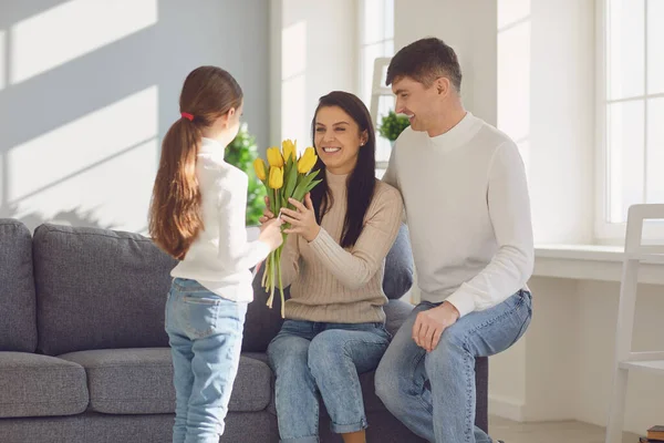 Gelukkige Moederdag. Vader en baby dochter feliciteert moeder met bloemen en een ansichtkaart in een kamer — Stockfoto