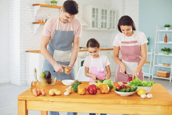 Familia feliz con el niño preparando verduras frescas en la mesa en la cocina . — Foto de Stock