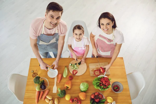 Famille heureuse avec enfant préparant des légumes frais sur la table dans la cuisine . — Photo