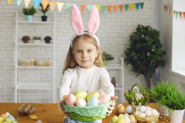 Boldog Húsvétot! Egy nyuszifülű kislány húsvéti tojást tart a kezében egy díszített szobában.. — Stock Fotó